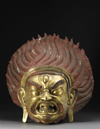 Testa di divinità in bronzo dorato, il volto dall'espressione feroce, una...