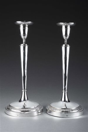 Coppia di candelieri in argento a corpo liscio cesellati sui bordi a motivi...