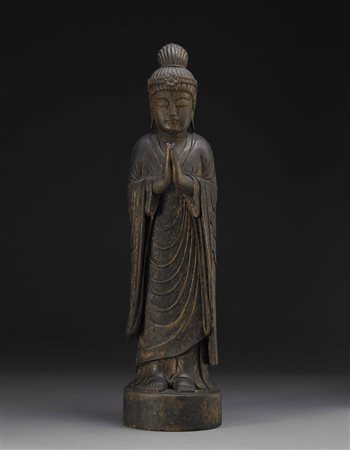 Scultura in legno intagliato raffigurante un Buddha stante, le mani giunte,...