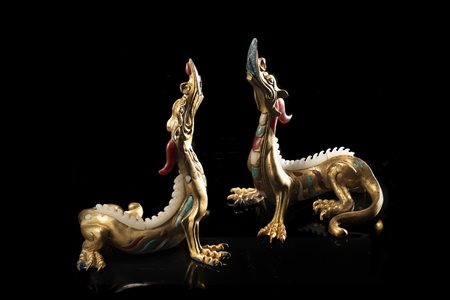 Coppia di draghi in metallo dorato, dalla forma longilinea e con il collo...