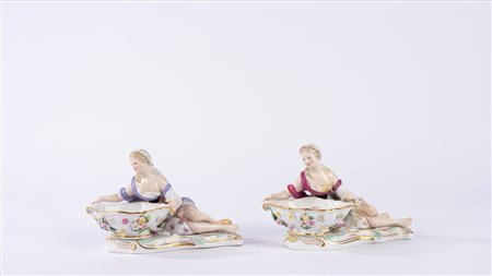 Coppia di saliere o salsiere in porcellana policroma in forma di fanciulla sdraiata che sostiene una vaschetta decorata con fiori applicati in rilievo, su una base a rocaille. Manifattura di Meissen, fine secolo XIX/inizio secolo XX.