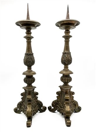 Coppia di portacero in bronzo con fusto tornito e decorato a foglie su base tri