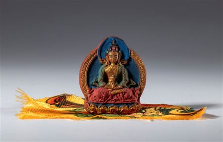  
Piccola Tza tza in argilla dipinta avvolta da un frammento di tessuto di seta  per il culto quotidiano buddista. Tibet o Nepal, XX secolo 
 mm 40.5 x 35.2 x 12