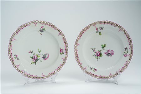 Coppia di piatti in porcellana a profilo traforato con fiorellini, decorati in policromia nei toni del porpora e del verde a rami di fiori. Manifattura di Berlino, 1770 circa