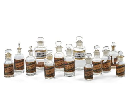 Tredici bottiglie da farmacia in vetro incolore con etichette cartacee e placch