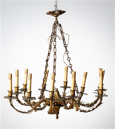Lampadario a dodici luci in metallo dorato con bracci e decori a volute fogliat
