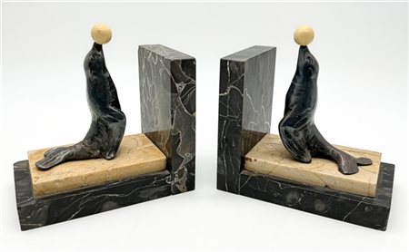 Coppia di fermalibri in marmi vari sormontati da figure di foca con sfera in ba