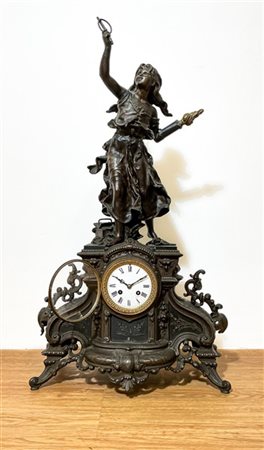 Pendola da appoggio in metallo sormontata da figura a tutto tondo. Quadrante in