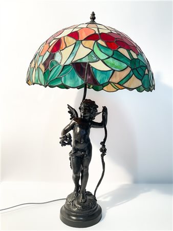 Lampada in fusione metallica e tessere di vetro con base in forma di putto. Ita