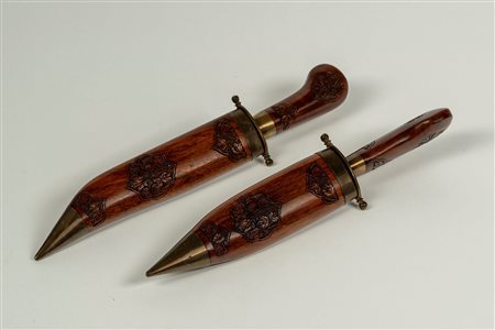Set da arrosto composto da forchettone e coltello in custodia a forma di pugnali in legno inciso a motivi floreali e metallo. Manifattura indiana secolo XX