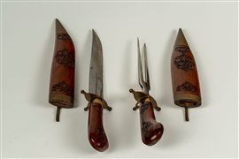 Set da arrosto composto da forchettone e coltello in custodia a forma di pugnali in legno inciso a motivi floreali e metallo. Manifattura indiana secolo XX