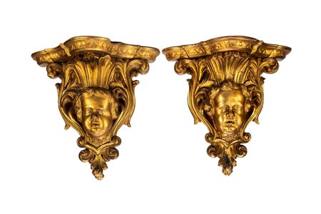 Coppia di console pensili in legno intagliato e dorato con sostegno a testa di putto tra volute di foglie. Secolo XIX