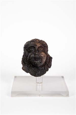 Elemento decorativo in pietra raffigurante volto con capigliatura a riccioli spiraliformi.