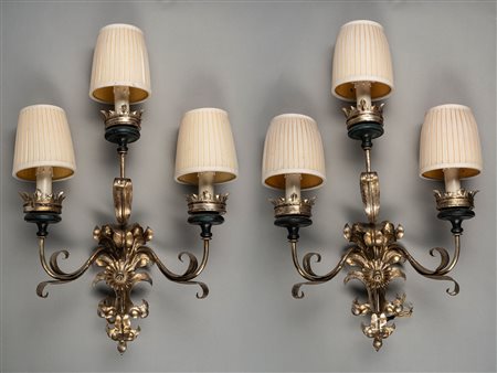 Coppia di appliques in metallo argentato a tre luci con bracci mossi a volute di foglie e fiori