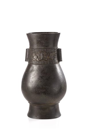 Vaso in bronzo di forma arcaica hu con anse tubulari e decorato con maschere...